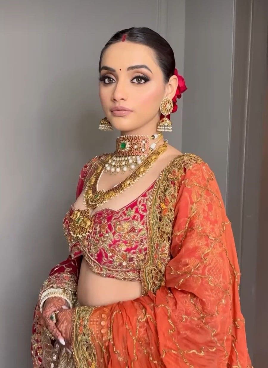 Bride in an orange lehenga with a red lip and gold jewellery